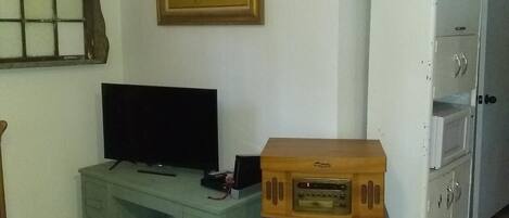 Une pièce comprenant un bureau en bois, un téléviseur, une armoire blanche et une petite table avec une radio.