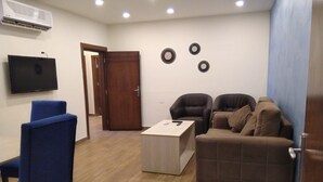 A living room with a flat-screen TV, a wooden coffee table, two armchairs, and a sofa.