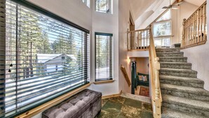 A spacious room with large windows, a wooden staircase, and a bench. - Sugar Pine Lodge: Hot Tub, Large Yard, Games (South Lake Tahoe)
