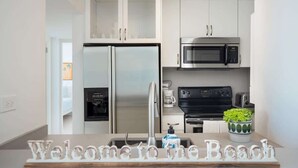 A modern kitchen with white cabinets, a stainless steel refrigerator, a microwave, and a coffee maker.