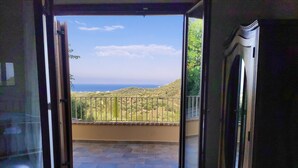 A room with a sliding glass door leading to a balcony with a view of the sea and hills. - Mastrogiannis villa Myrtia (Kavvadades)