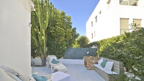 Een terras met witte loungestoelen, een decoratieve bank en een cactus.