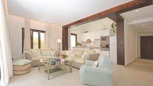 Een moderne woonkamer met een bank, fauteuil en salontafel, verbonden met een keuken met witte kasten en apparatuur.