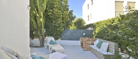 A sunlit patio with lounge chairs, a cactus, and a stone wall.