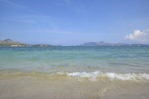 A beach with clear water, a sandy shore, and distant mountains.