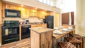 A modern kitchen with wooden cabinets, a granite countertop, and a built-in island with bar stools. - Gold Camp Silver Strike Condo: On Shuttle Route (Breckenridge)