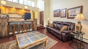 A spacious living area with a leather sofa, a coffee table, and a kitchen in the background. - Gold Camp Silver Strike Condo: On Shuttle Route (Breckenridge)