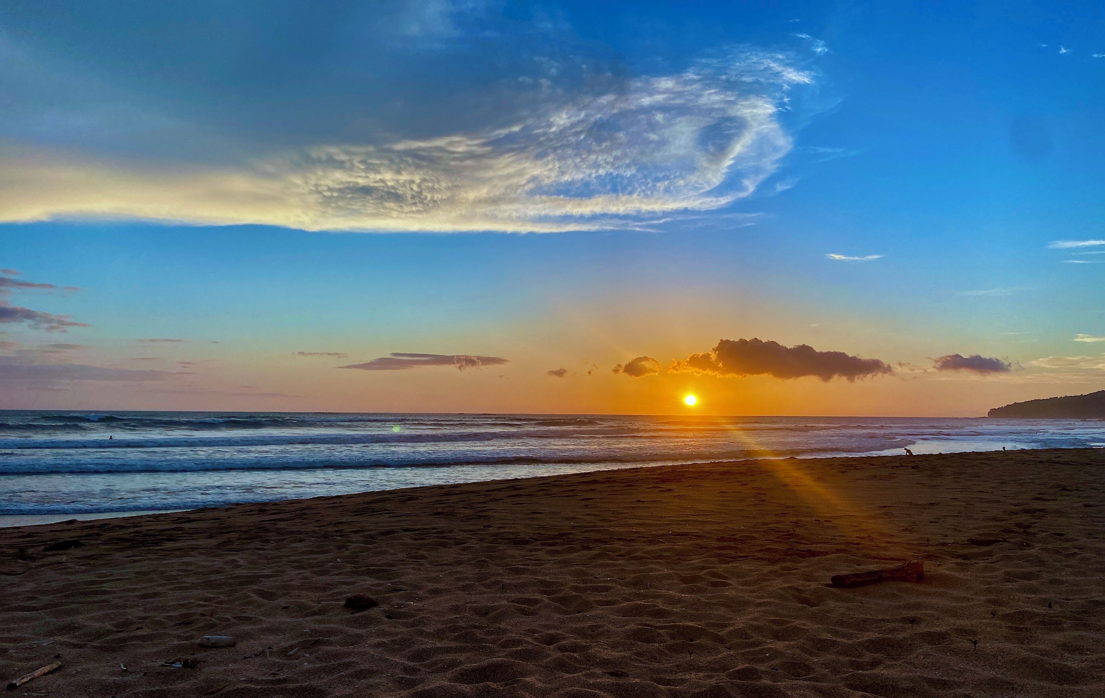 A beach with the sun setting over the horizon, casting rays of light onto the sand.