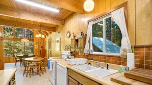 Une cuisine rustique aménagée dans une cabane en bois, avec une table à manger en bois, des chaises, un four encastré, un évier et une fenêtre avec des rideaux.