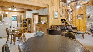 Un intérieur de chalet chaleureux comprenant un coin repas, un salon avec cheminée, des murs en bois et un mur d’accent en pierre.