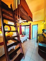 Una habitación con escalera de madera, dos camas con ropa de cama estampada, un ventilador de techo y una ventana con cortinas.