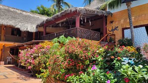 Un edificio con techo de paja, balcón y jardín con diversas flores.