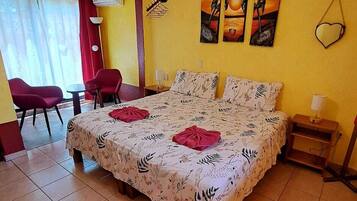 Ein Schlafzimmer mit einem Bett, Deckenventilator, einem Sessel, einem Tisch und Bildern an der Wand.