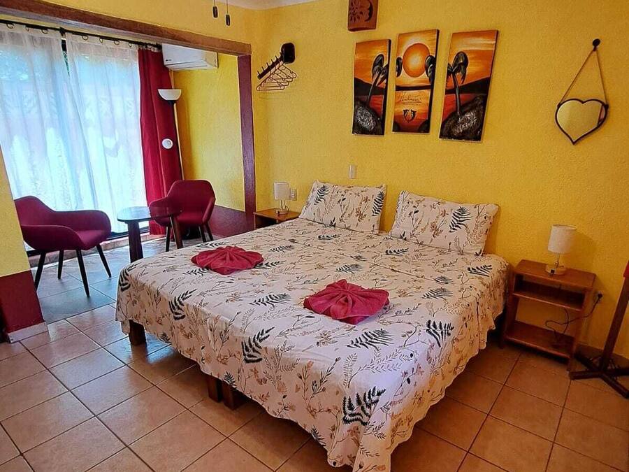 Ein Schlafzimmer mit einem Bett, Deckenventilator, einem Sessel, einem Tisch und Bildern an der Wand.