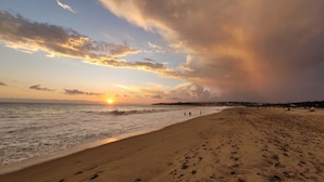 Una playa con huellas, olas y un atardecer.