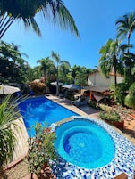 Una piscina con borde de mosaicos, rodeada de palmeras y sillones de descanso.