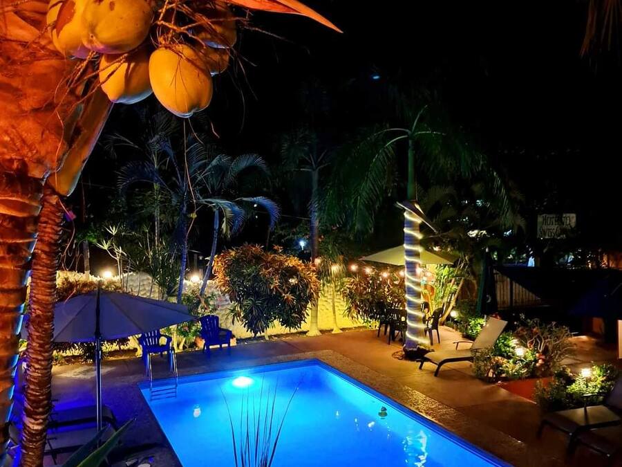A nighttime pool area with a clear pool, palm trees, and outdoor seating.