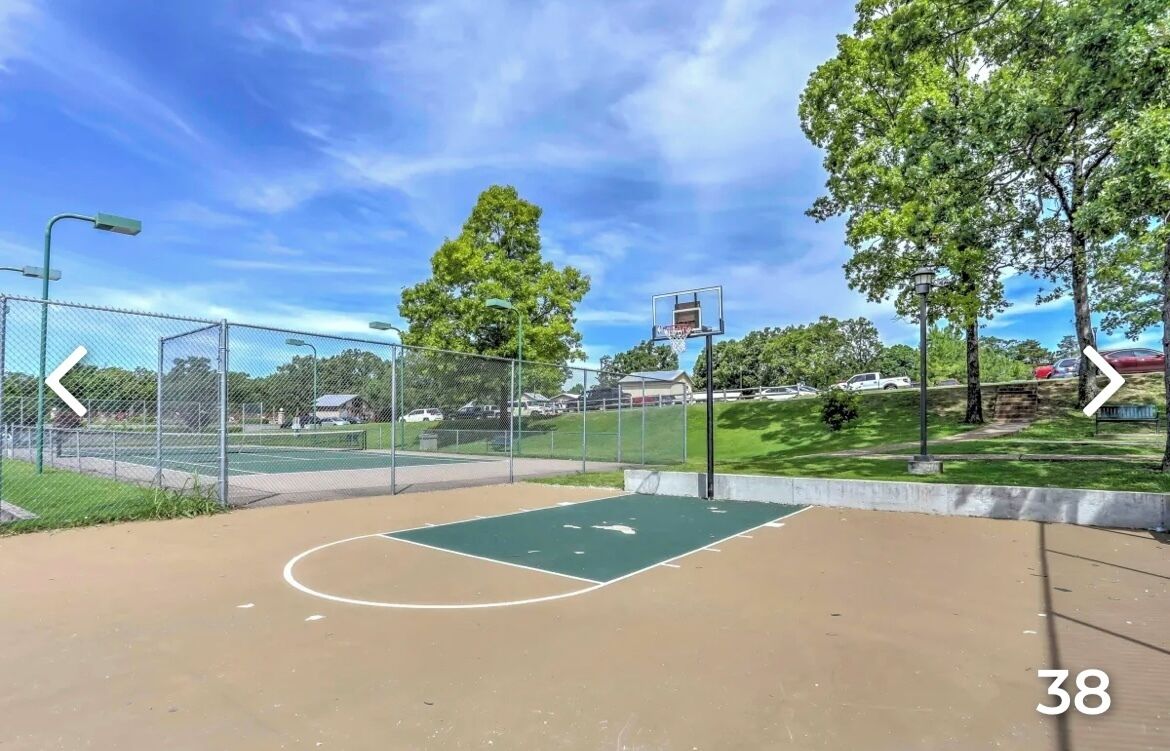 Un terrain de basket en plein air, entouré d’une clôture, avec des arbres et un ciel dégagé.
