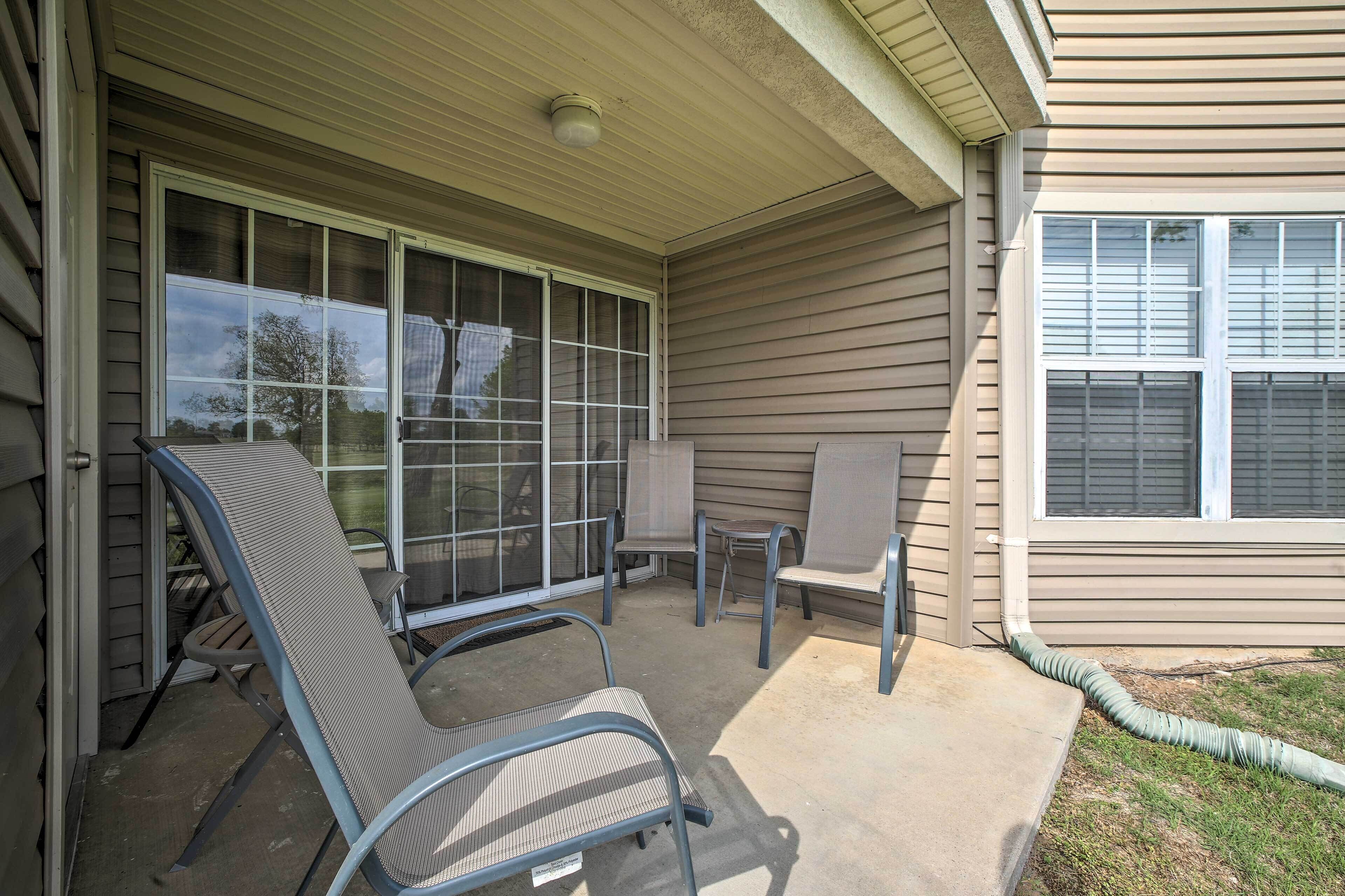 A covered patio area with two metal chairs and a table, a sliding glass door, and a window with blinds.