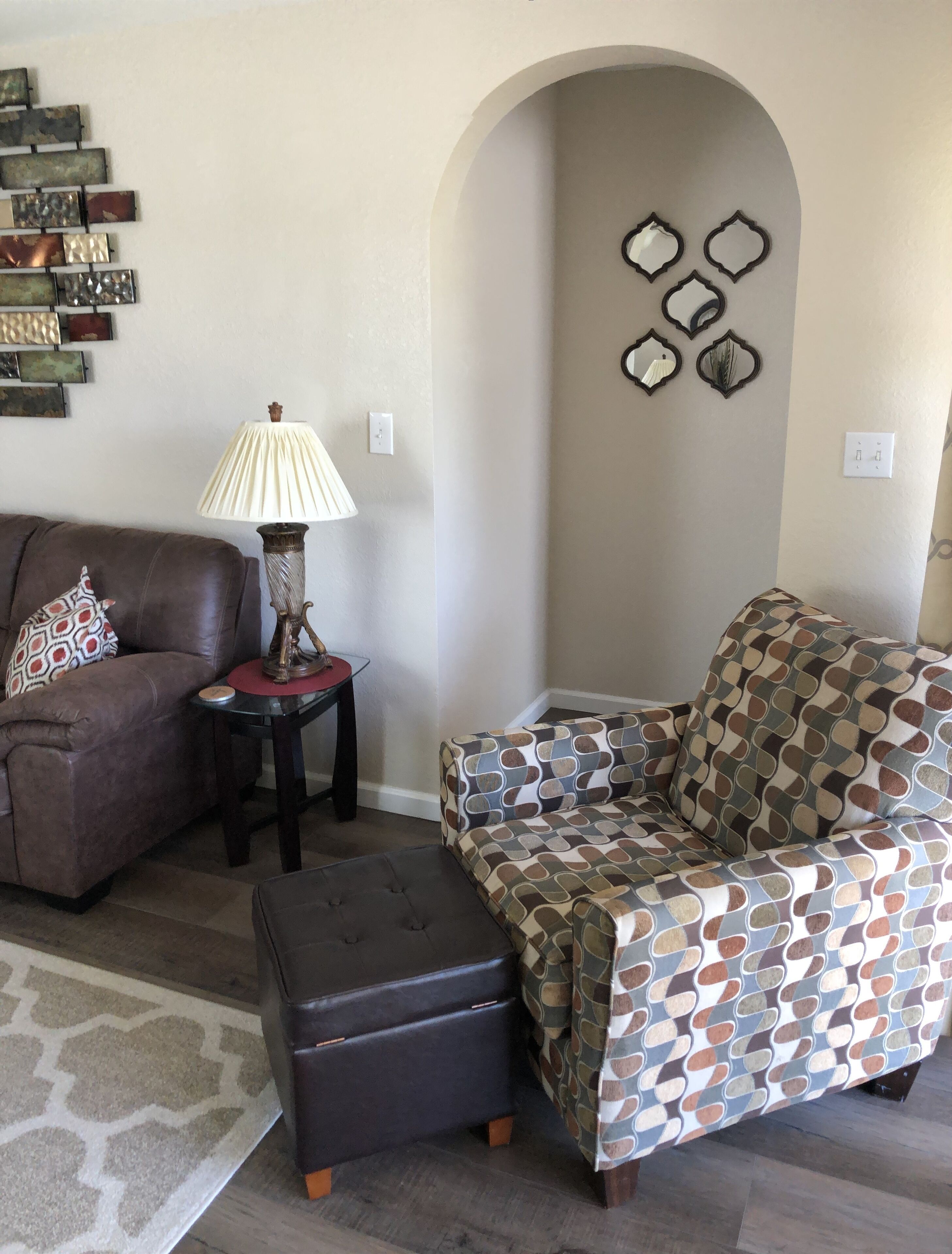 A living room with a brown leather sofa, a patterned armchair, a small table with a lamp, and decorative wall art.