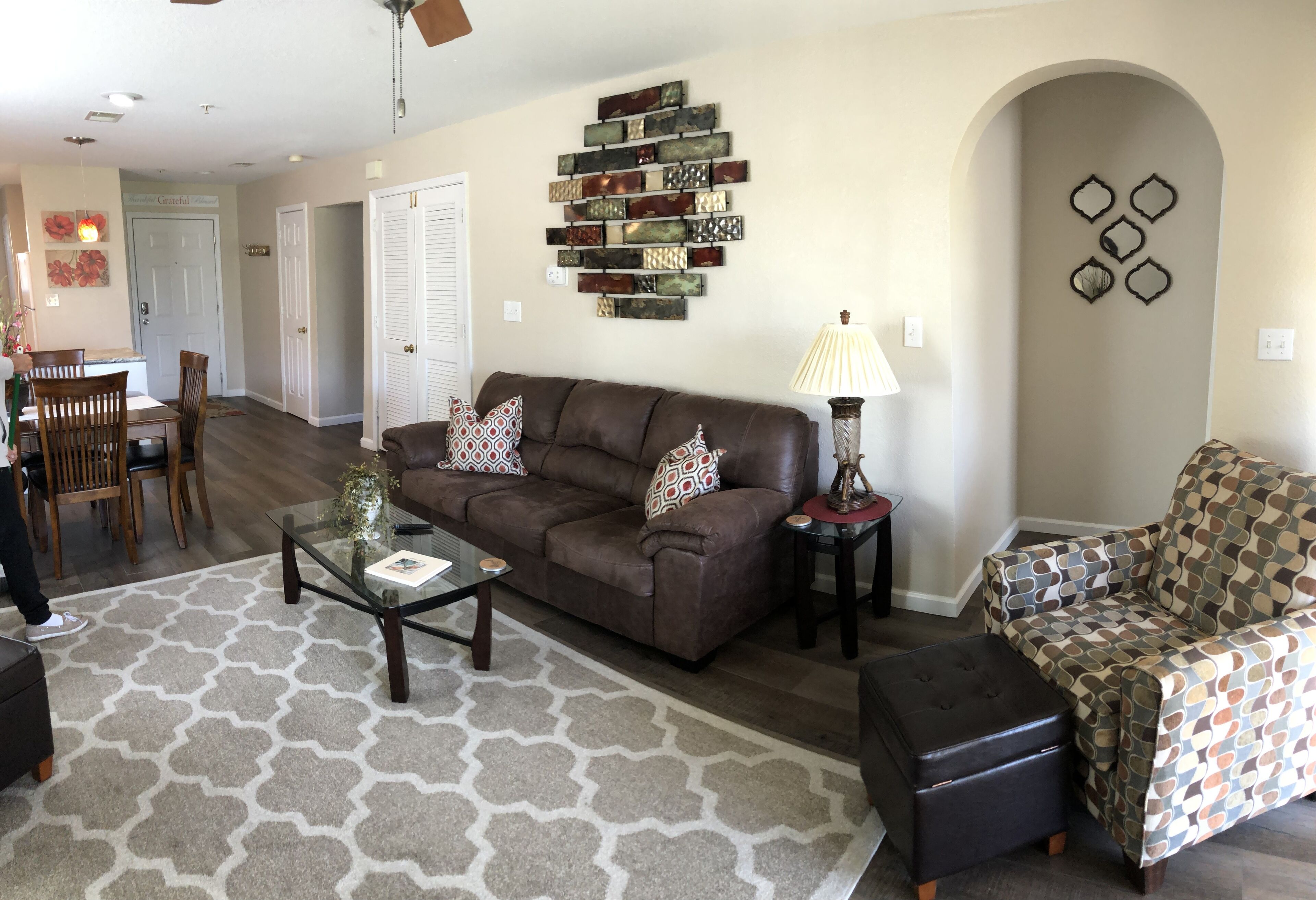 A living room with a brown leather sofa, patterned armchair, and a glass coffee table.