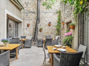 An outdoor patio with stone walls, wicker furniture, and potted plants. - L'Oiseau qui Chante (Eygalieres)