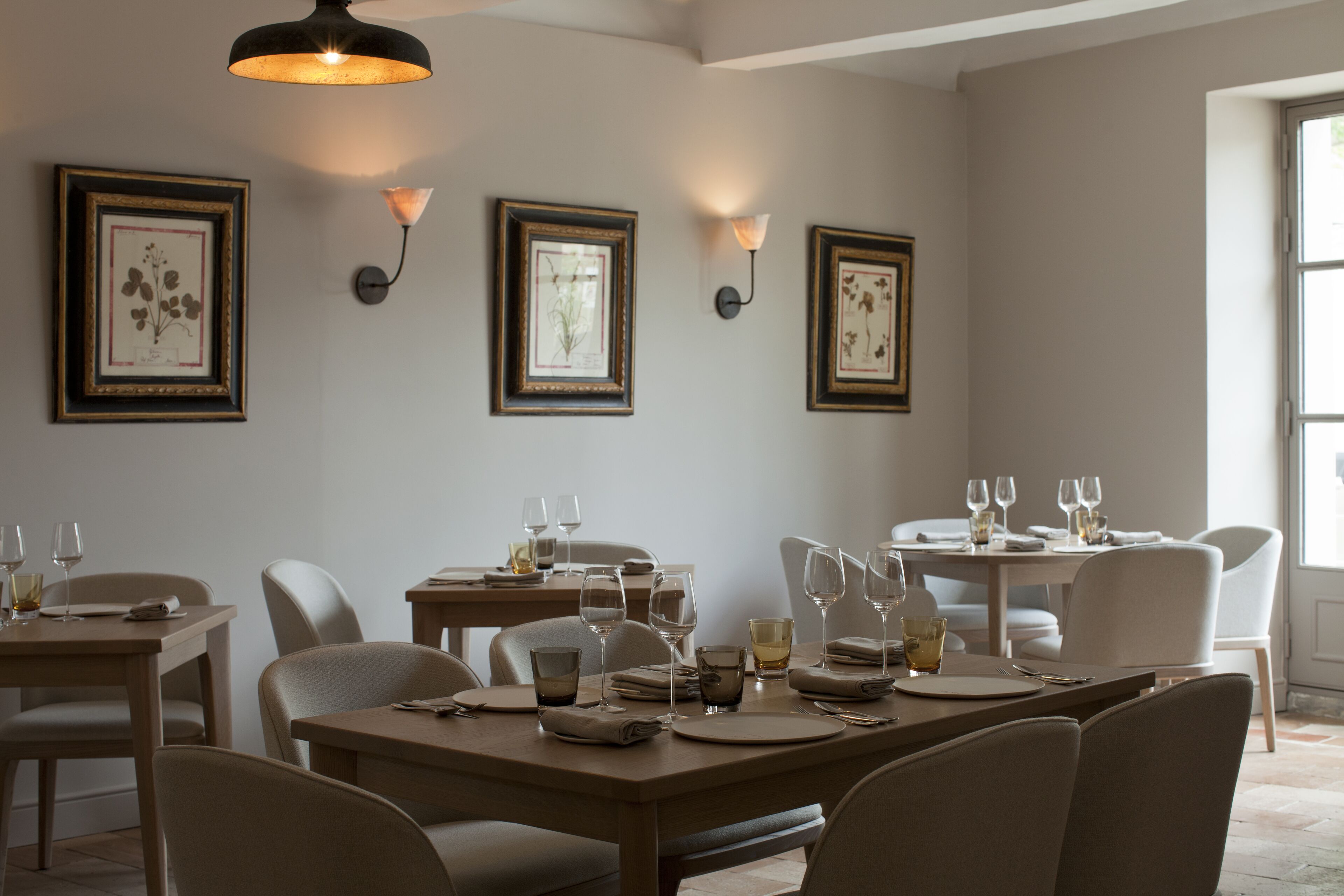 A dining area with tables set for four, framed artwork on the walls, and pendant lighting.