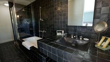 Un baño moderno con pared de azulejos negros, ducha con cerramiento de vidrio, bañera blanca y lavamanos con espejo.