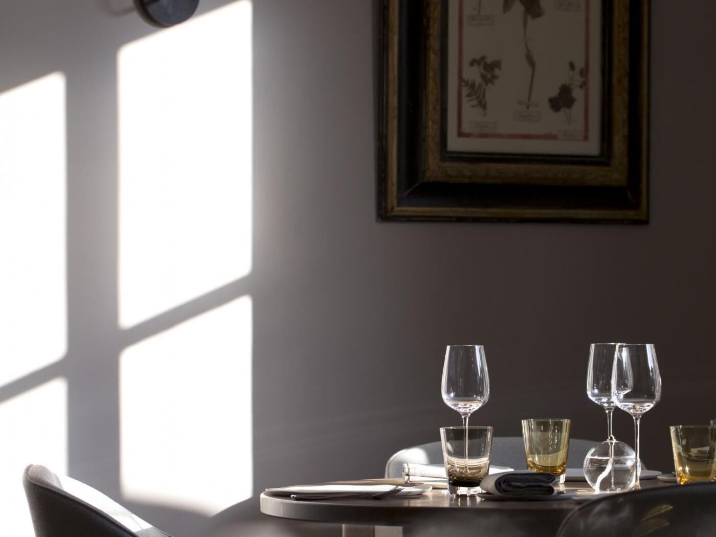 A dining table with wine glasses and a framed botanical illustration on the wall.