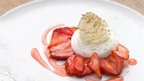Un dessert con base bianca, guarnito con una quenelle di crema e una spolverata di pepe nero, circondato da fragole a fette e salsa rosa.