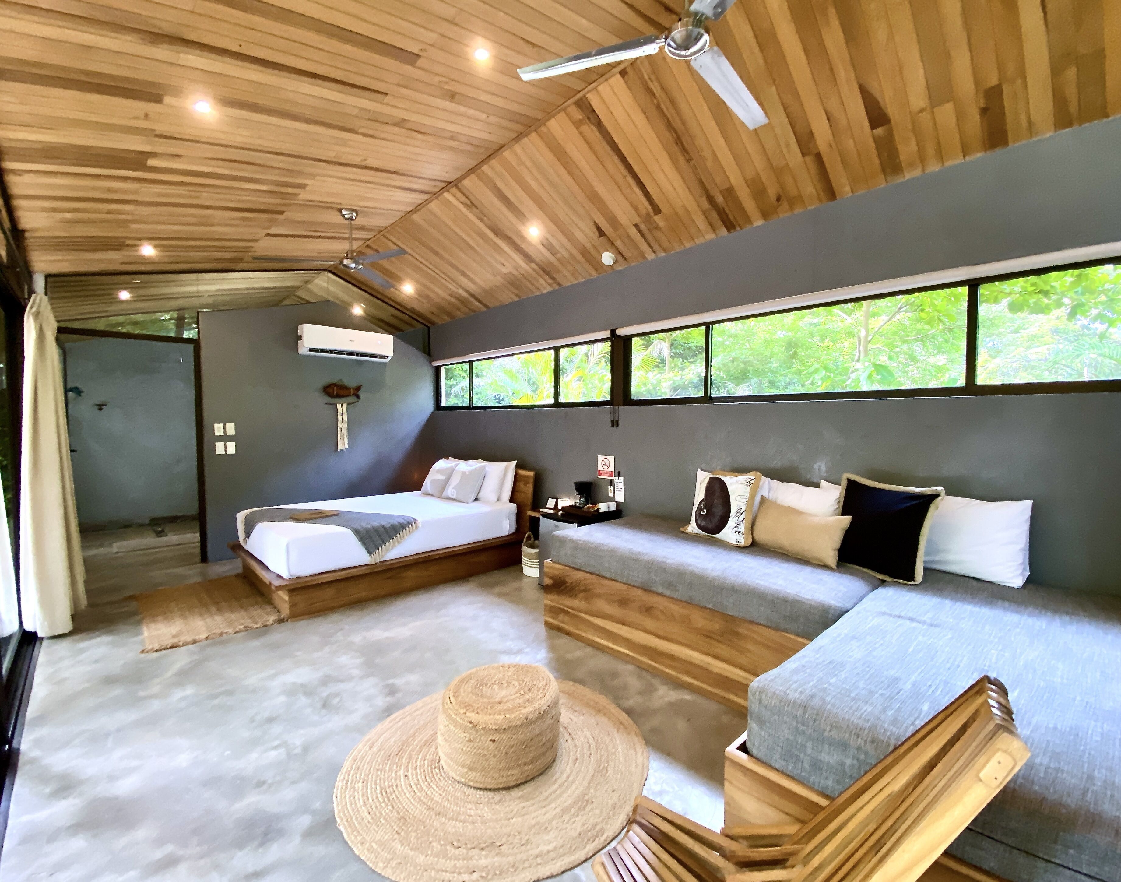 Une chambre avec deux lits, un canapé, un ventilateur de plafond et une grande fenêtre donnant sur un paysage verdoyant.