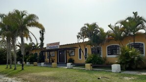 A building with a sign reading "POUSADA Samburá" surrounded by palm trees and a grassy area. - Samburá Chalets (Ilha Comprida)