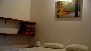 A hotel room with a bed, pillows, a painting on the wall, and a shelf with folded blankets. - Samburá Chalets (Ilha Comprida)