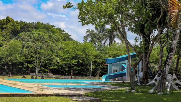 A swimming pool with a blue slide, surrounded by lush greenery and trees. - Samburá Chalets (Ilha Comprida)