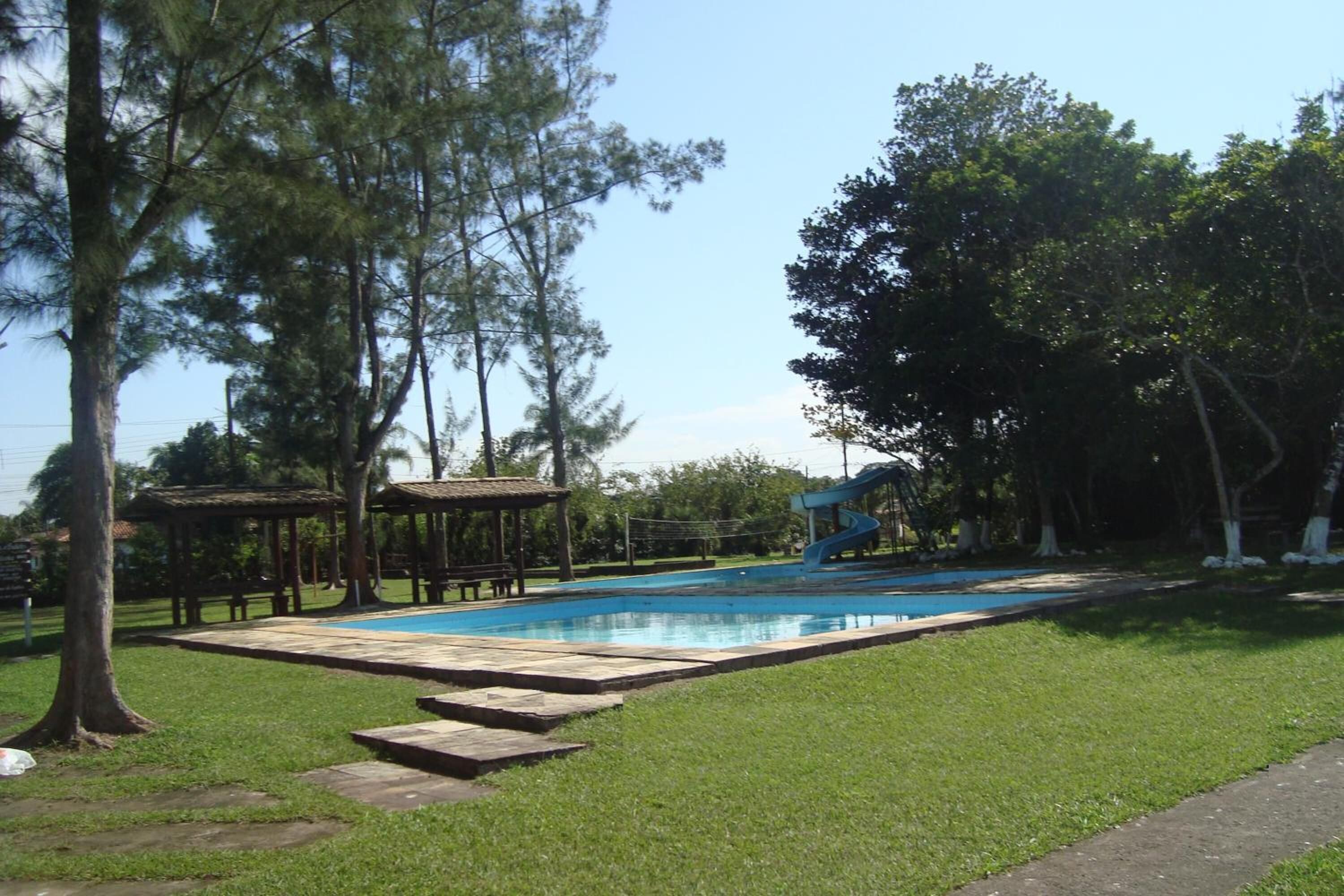 A swimming pool with a slide, surrounded by grass and trees.