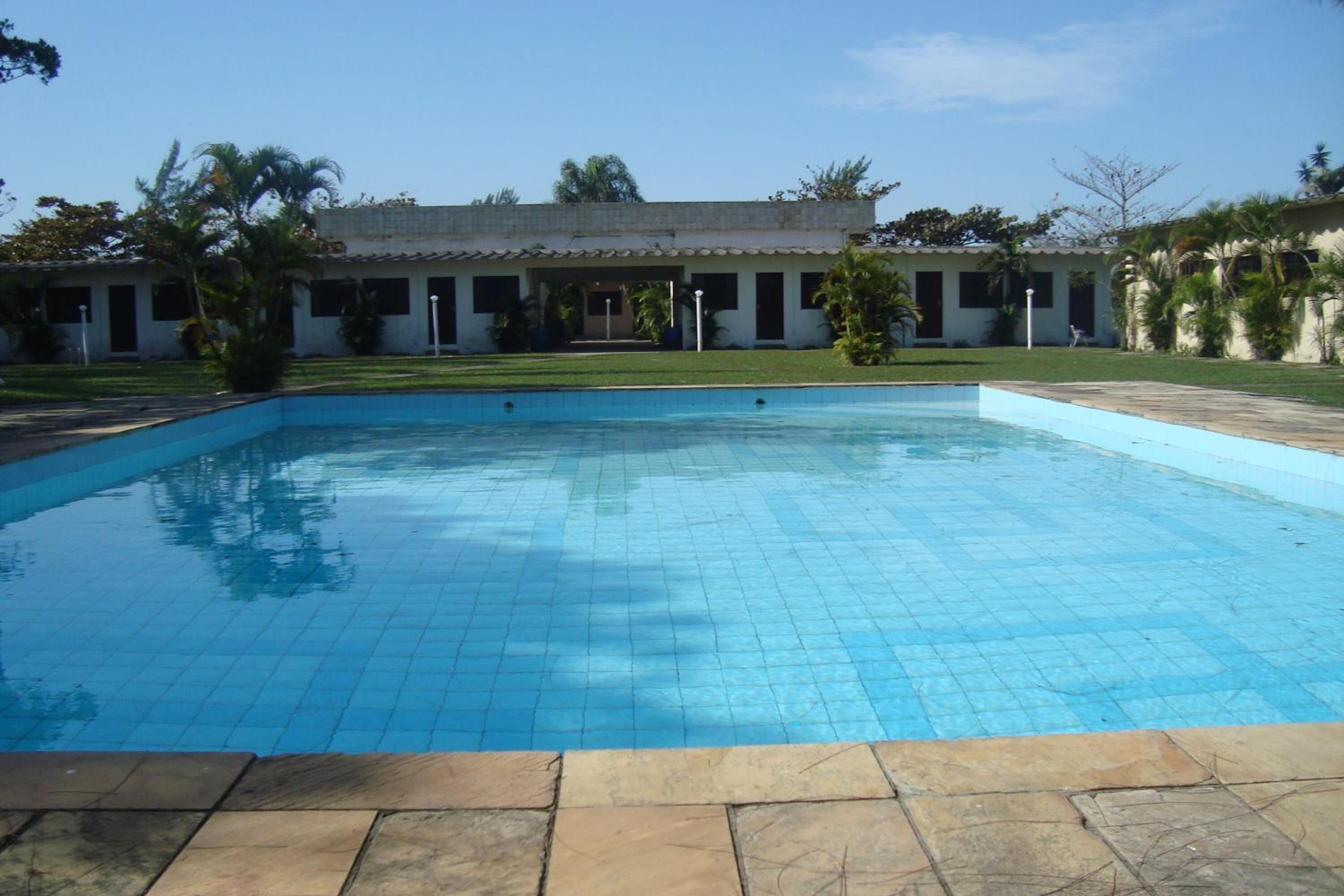 A swimming pool with tiled flooring, surrounded by a building with multiple windows and a covered patio area.