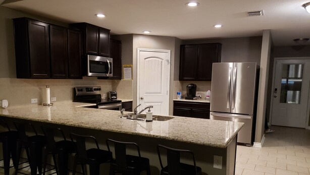 Una cocina moderna con armarios de madera oscura, electrodomésticos de acero inoxidable, encimera de granito y taburetes de bar.