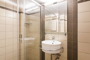 A modern bathroom with a glass shower enclosure, a white sink with a chrome faucet, and a mirror above the sink. - Acropolis - historical attractions walking distance (Athina)