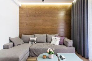 A modern living room with a sectional sofa, a coffee table with a vase of flowers, and a remote control. - Acropolis - historical attractions walking distance (Athina)