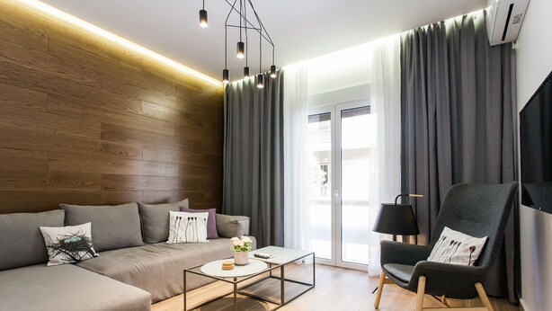 A modern living room with a sectional sofa, a glass coffee table, a dark armchair, and a large window with curtains. - Acropolis - historical attractions walking distance (Athina)