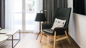 A modern living room with a grey armchair, a black floor lamp, and a flat-screen TV mounted on the wall. - Acropolis - historical attractions walking distance (Athina)