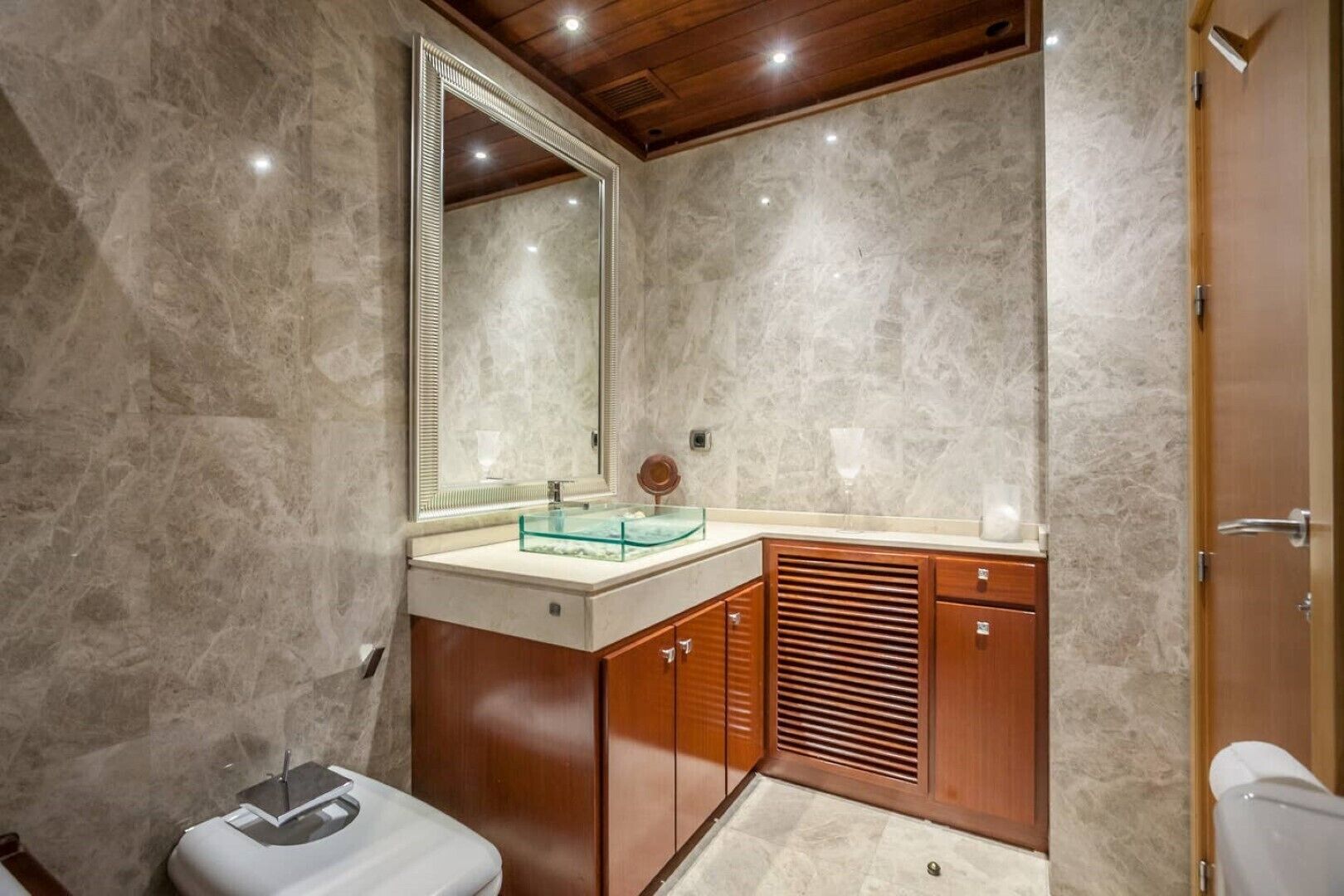 Un baño con pared de mármol, tocador de madera y un espejo grande.