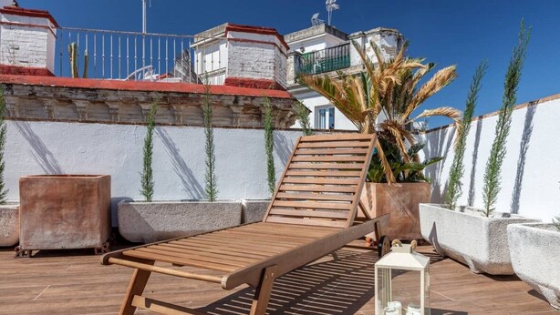 A wooden lounge chair on a tiled patio with potted plants and a white lantern. - Duplex penthouse with 70 m terrace (Sevilla)