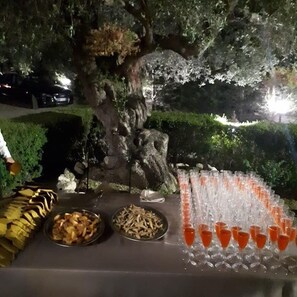 An outdoor dining setup with a table set for a meal, including bowls of food and a row of glasses filled with a red beverage. - Casale degli Ulivi (Ciro Marina)