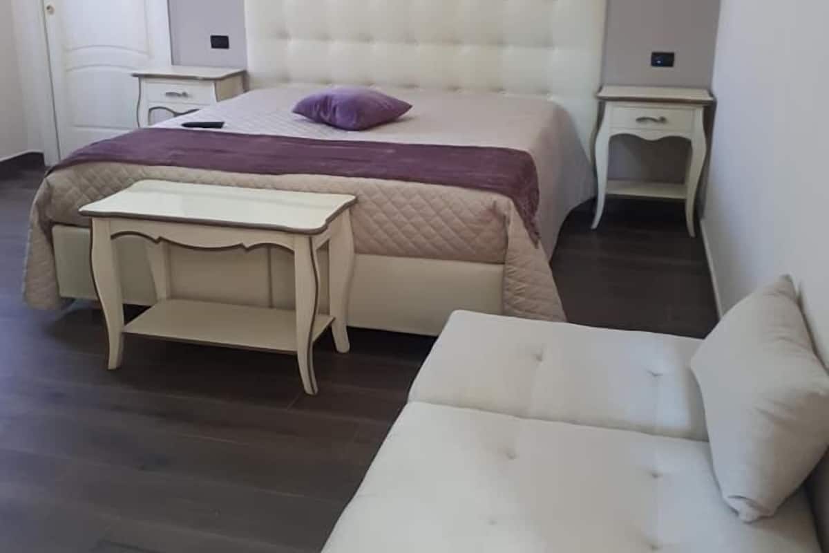 A bedroom with a bed, bedside tables, a nightstand, a dresser, and a sofa.