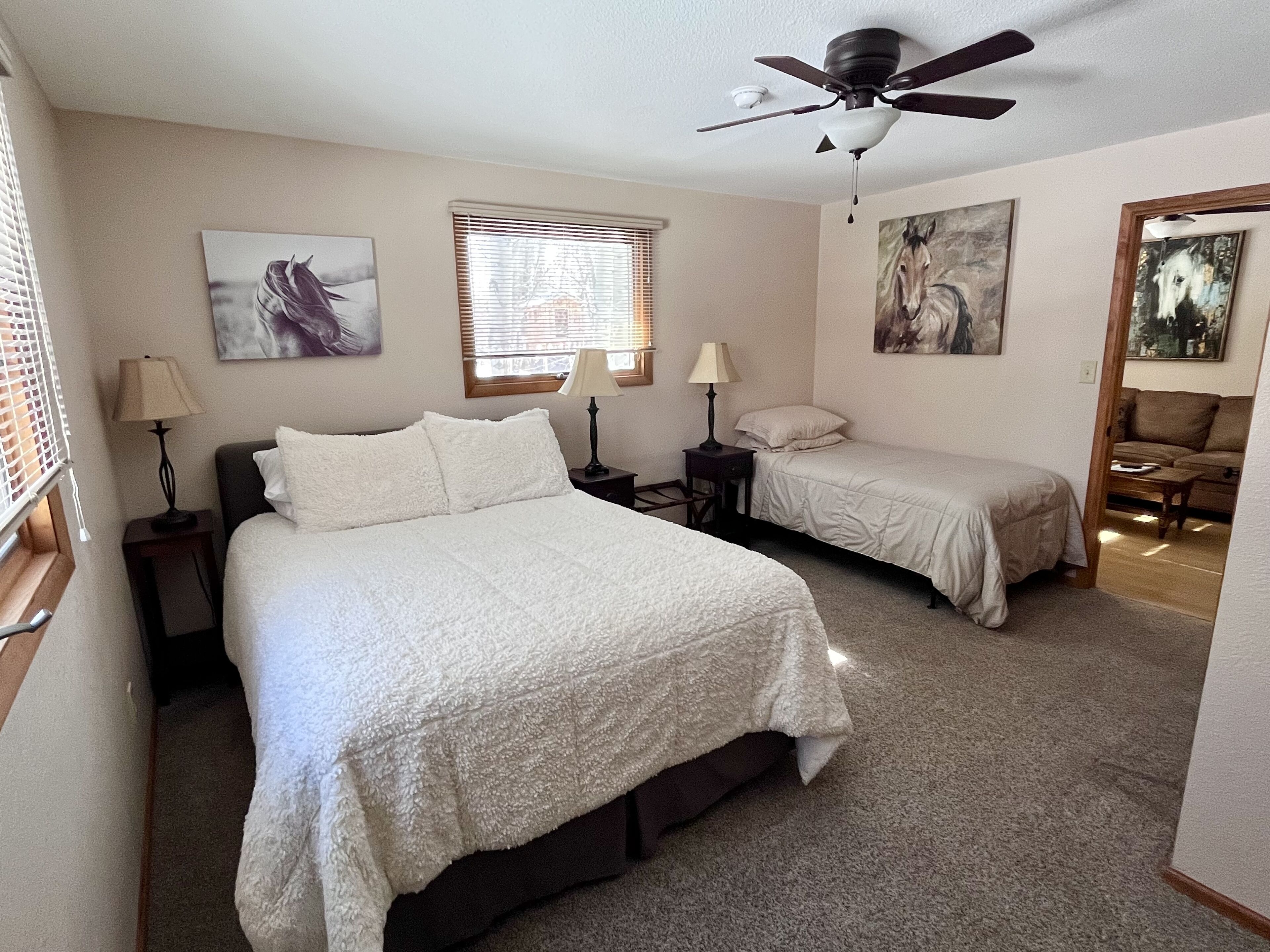 A bedroom with two beds, a ceiling fan, and artwork on the walls.