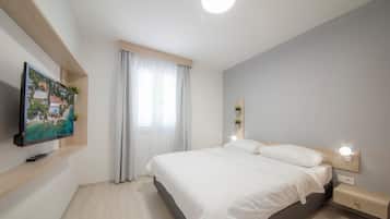 Un dormitorio moderno con cama, mesitas de noche, televisor montado en la pared y ventana con cortinas.