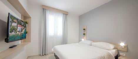 A modern bedroom with a bed, bedside tables, a TV mounted on the wall, and a window with curtains.