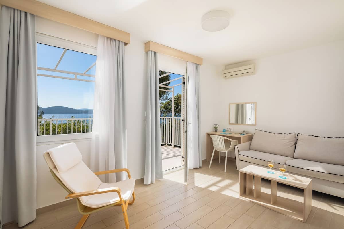 A modern living room with a balcony, a sofa, a chair, a small table, and a desk with a chair.