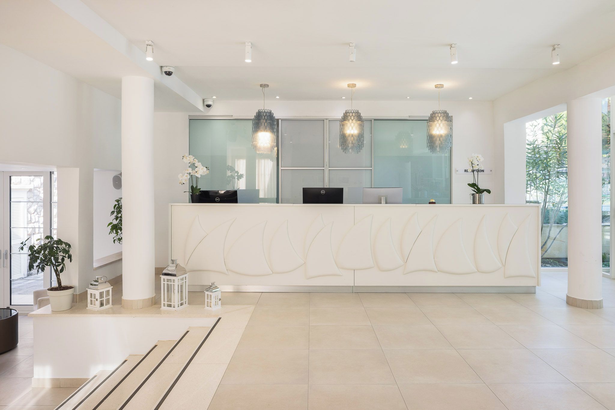 Una moderna zona de recepción con un mostrador blanco, dos computadoras de escritorio e iluminación decorativa.